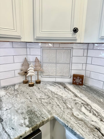 a set of four white, handmade tree tiles installed in the corner of a kitchen backsplash