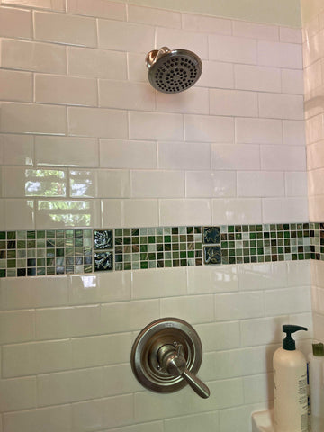 close up of a tiled shower with white subway tiles and a green stripe of glass and handmade feature tiles