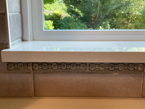 a row of gray handmade tiles with pattern featuring circles installed over a kitchen sink and under a window