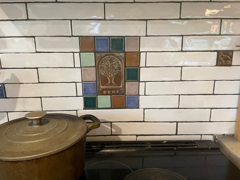 white subway tiles installed over a kitchen stove with an art tile insert featuring multi-colored handmade tiles