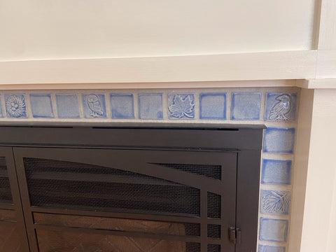 close up of small handmade tiles installed in a hearth. Tiles are light blue and feature plants and animals.