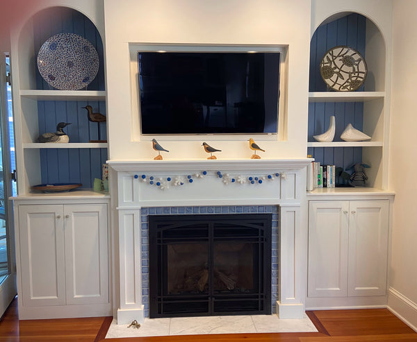festive blue and white hearth with small handmade tiles installed. Tiles are light blue and feature plants and animals. Hearth is surrouned by built in shelves