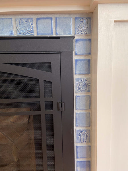 close up of small handmade tiles installed in a hearth. Tiles are light blue and feature plants and animals.