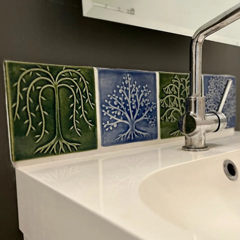 handmade tree tiles in blue and green glaze installed over a white bathroom sink