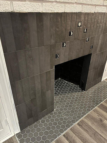 handmade tiles depicting the phases of the moon installed among black tiles around a fireplace