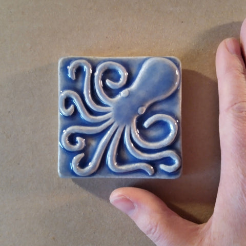 3x3 inch octopus handmade tile in watercolor blue glaze with artists hand in the frame for size reference
