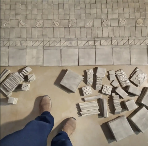 gray handmade tiles spread out on the floor of the studio so they can be packed and shipped