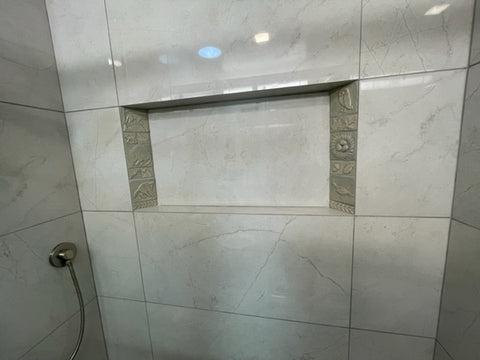 a tiled shower niche that features handmade tiles on the sides