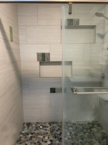 a modern bathroom featuring large, white tiles, interspersed with handmade tile accents