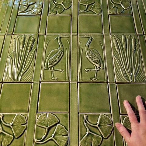 light green handmade tiles depicting herons, cattails and ginkgo leaves