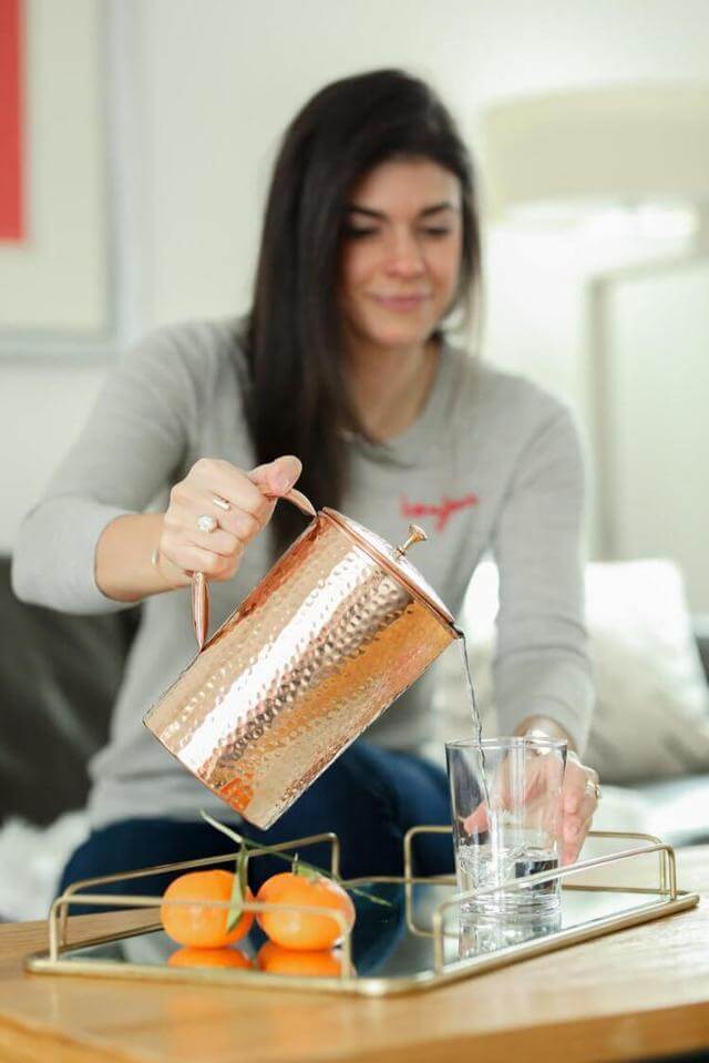 woman pouring water from a Shantiva copper pitcher into a glass