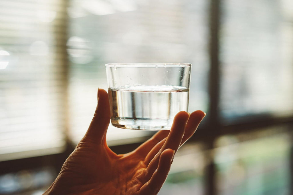 hand holding a small clear glass of half-filled water