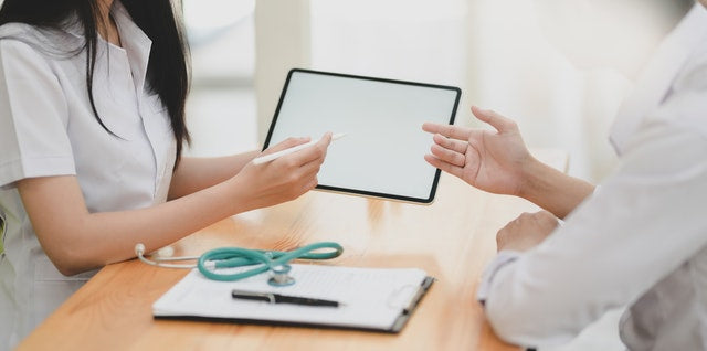 woman holding a tablet with stethoscope, clipboard and pen on the table 