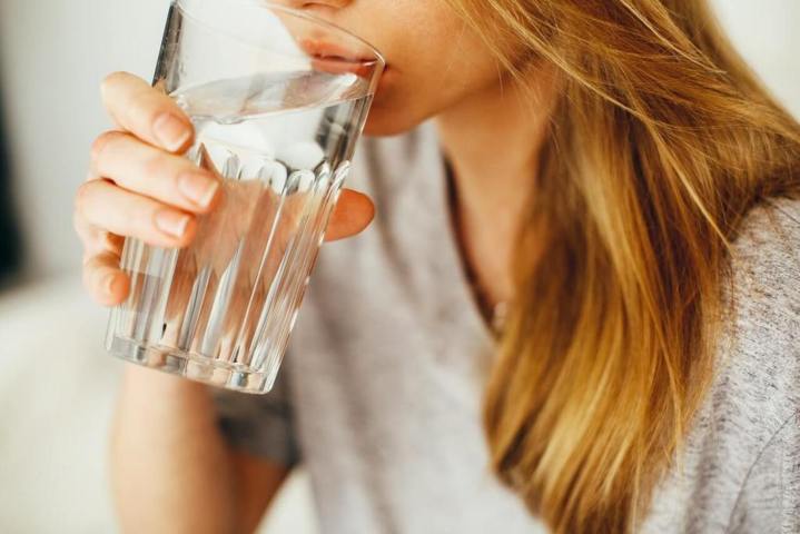 woman wearing gray shirt drinking water from a glass