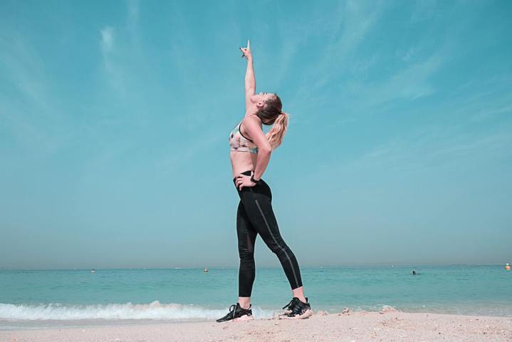 woman in athletic wear pointing upward standing on the beach shore