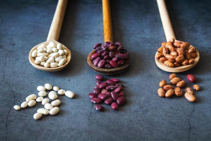 three wooden spoons containing white red and yellow beans