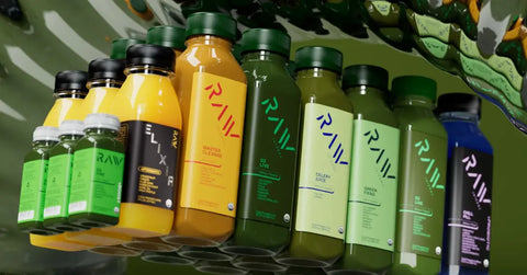 Cold-pressed juice selection from Raw Juicery displayed in a mirrored, artistic composition.