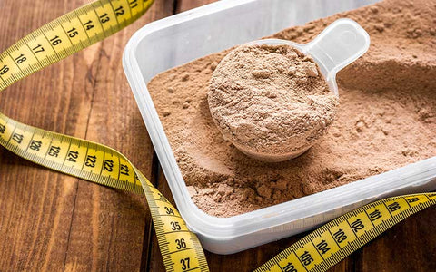 Protein shake powder in a scoop and measuring tape on a wooden background