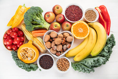 Healthy food set against a white background featuring bananas, nuts, seeds, broccoli, tomatoes, peppers, and more