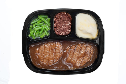 An unhealthy Salidbury steak TV dinner with gravy, mashed potatoes and a brownie dessert in a plastic tray isolated on white background