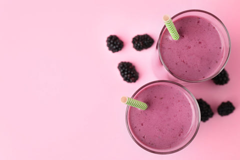 Blackberries next to a blackberry smoothie against a pink background