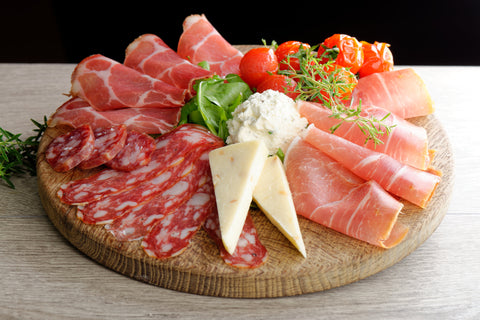 Arrangement of deli cold cuts on a wooden plate with ham, cheese, pepperoni, and salami