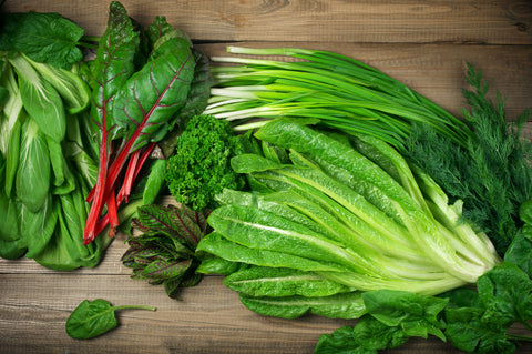 Various green leafy vegetables on rustic wooden table