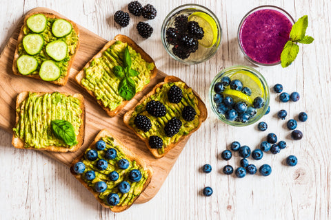 Blackberries, blueberries, and other veggies and fruit on an avocado toast against a white backdrop