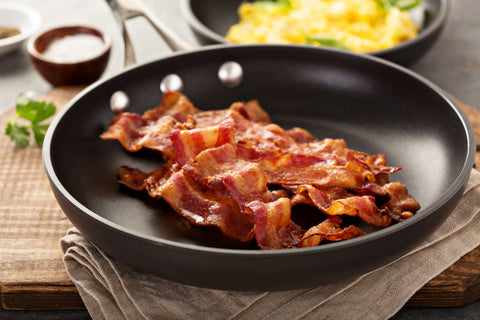 Cooked sizzling hot crispy bacon on a skillet and scrambled eggs ready for breakfast