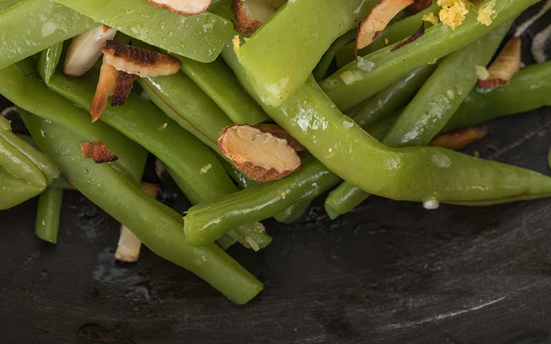 Green beans with almonds on a black background.