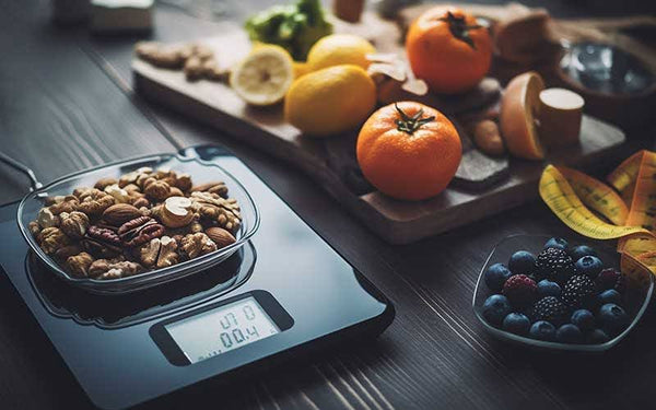 Healthy bowls of organic fruits and nuts, a weight scale, and measuring tape.