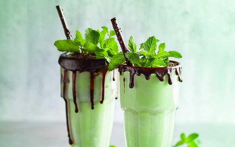 Chocolate shake with fresh mint leaves in glass on a green background.