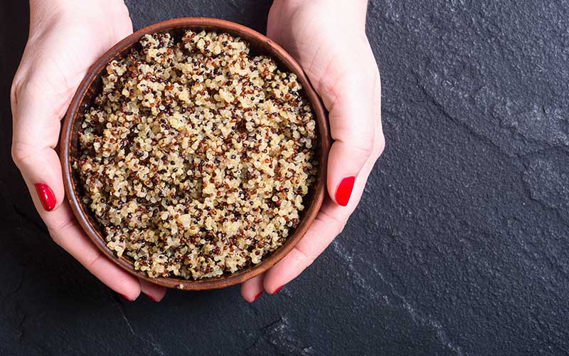 A bowl of healthy quinoa in a woman's hand on a dark background.