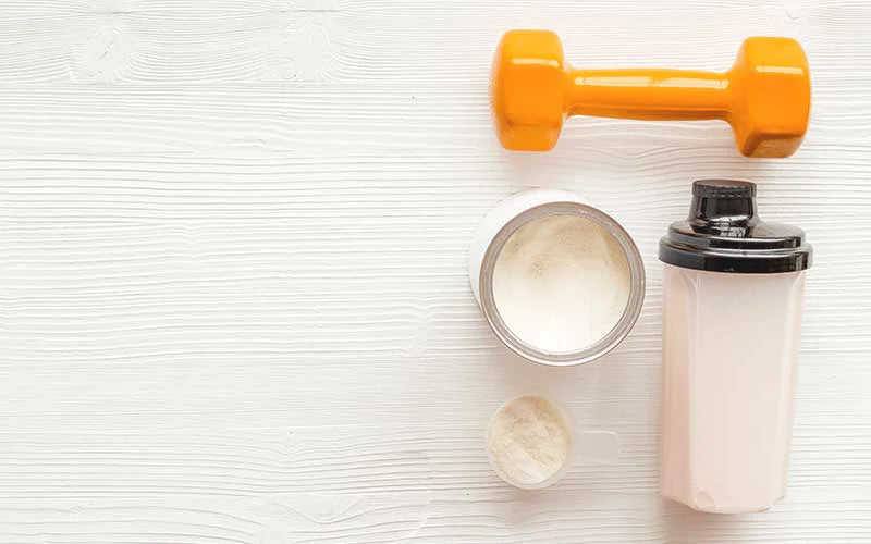 Protein shake near dumbbells on white background