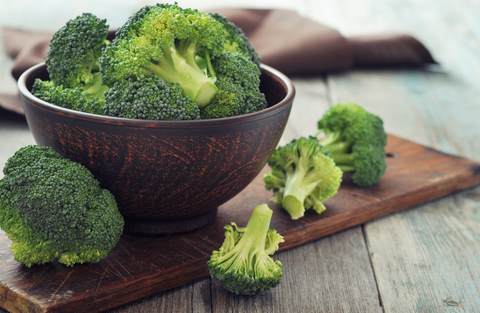 Bunch of fresh green broccoli in brown bowl over wooden background