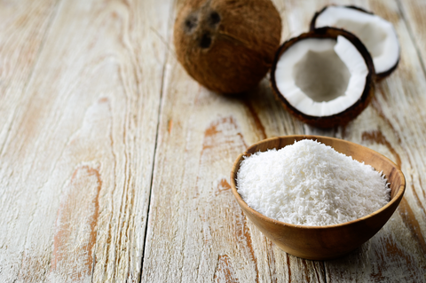 Grated coconut in bowl with its shell on background