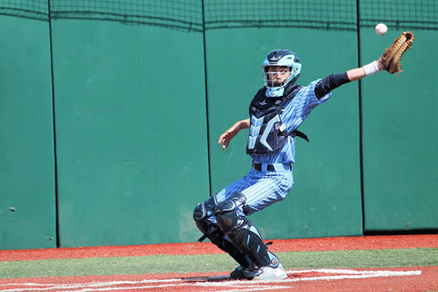 Baseball catcher in full gear reaching to catch a baseball.