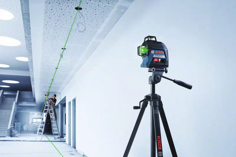 Laser Level on a tripod in a long white room, man follows guide on a ladder on the opposite side