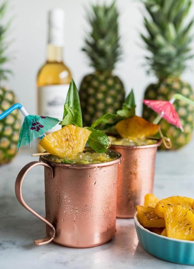 two copper mugs filled with ice and pineapple and mint leaves wedged on the rim