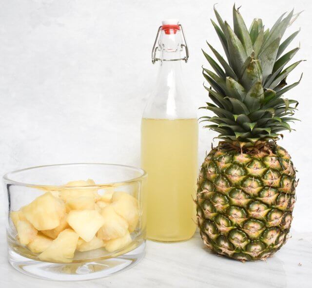 pineapple cubes placed in a clear glass jar beside a bottle and pineapple