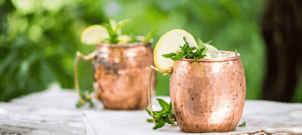 two Moscow Muled mugs filled with drink, mint leaves and slice of lemon