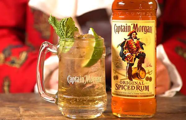 clear mug filled with liquid ice mint leaves and lime slices beside Captain Morgan Original Spiced Rum bottle