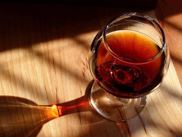 brown liquid filled in a snifter glass placed on a wooden surface