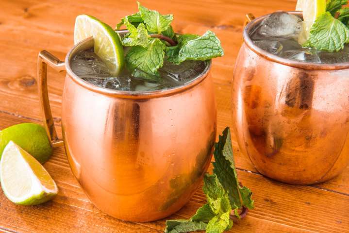 two copper mugs filled with liquid ice and mint leaves placed on a wooden surface