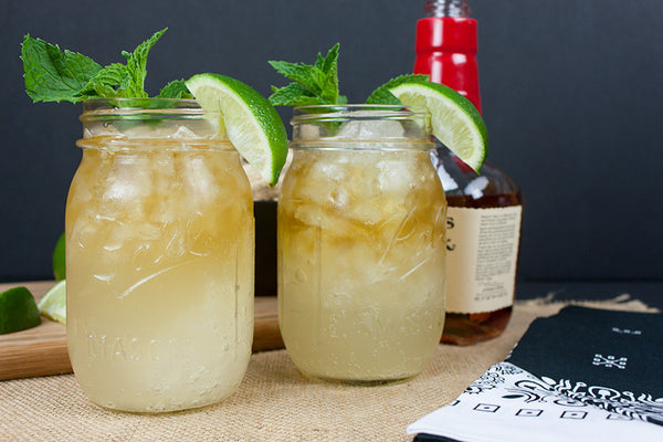 two clear Mason jar glass filled with yellow beverage ice mint leaves and citrus slice