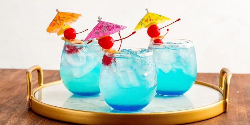 three clear glasses filled with blue liquid ice cubes and tiny umbrella 