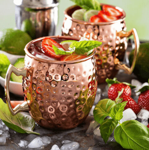 two Moscow Muled copper mugs filled with liquid strawberry ice and mint leaves