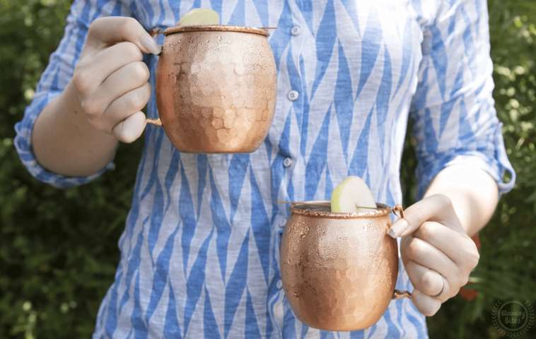 person wearing blue clothes carrying two Moscow Muled copper mugs in each hand