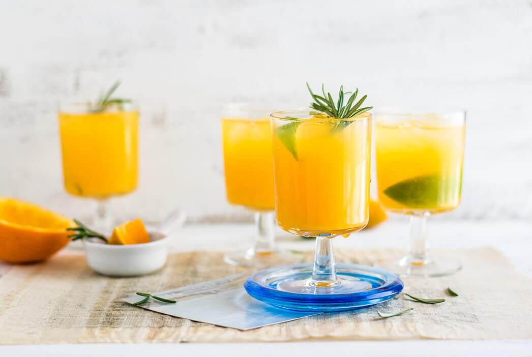 four clear glasses with stems filled with yellow liquid