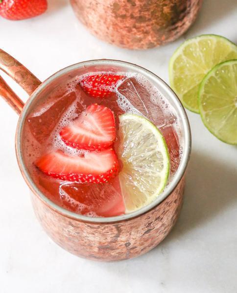 copper mug filled with pink liquid slices of strawberry lime and ice